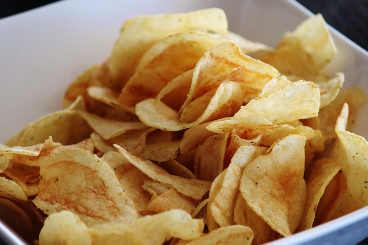 A close-up of a white bowl filled with crispy, golden potato crisps, showing their thin, curved texture—perfect for those seeking healthy snacks or exploring tasty crisp alternatives.