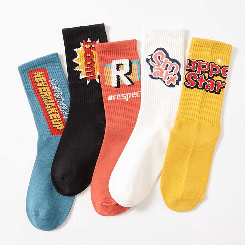 Five colourful socks with playful, comic-style designs and words like "SUPERSTAR," "RESPECT," and "SUPPORT" on them, arranged side by side on a white background.