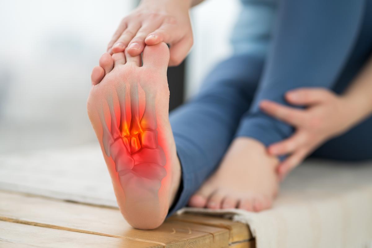 A person holding their foot, with a red highlighted area on the sole indicating pain from plantar fasciitis in the arch, suggesting discomfort or a foot injury.