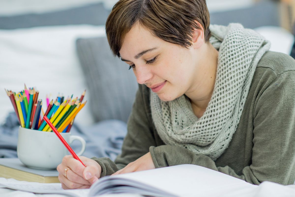A woman colouring in a book, enjoying a moment to de-stress—perhaps jotting down thoughts or laughing over sweary colouring books.