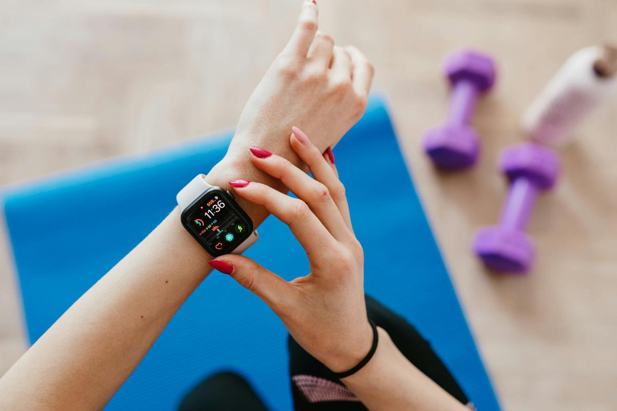 A person wearing a wearable fitness tracker checks their stats while sitting on a blue exercise mat. Purple dumbbells and a water bottle are nearby, suggesting a workout session inspired by an unbiased guide to fitness trackers 2026.