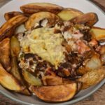A bowl of spicy Cajun potato wedges arranged around a hearty mixture of minced meat, vegetables, and melted cheese, served on a wooden surface for a flavourful and healthy meal.