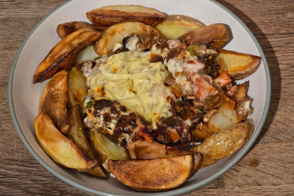 A bowl of spicy Cajun potato wedges arranged around a hearty mixture of minced meat, vegetables, and melted cheese, served on a wooden surface for a flavourful and healthy meal.