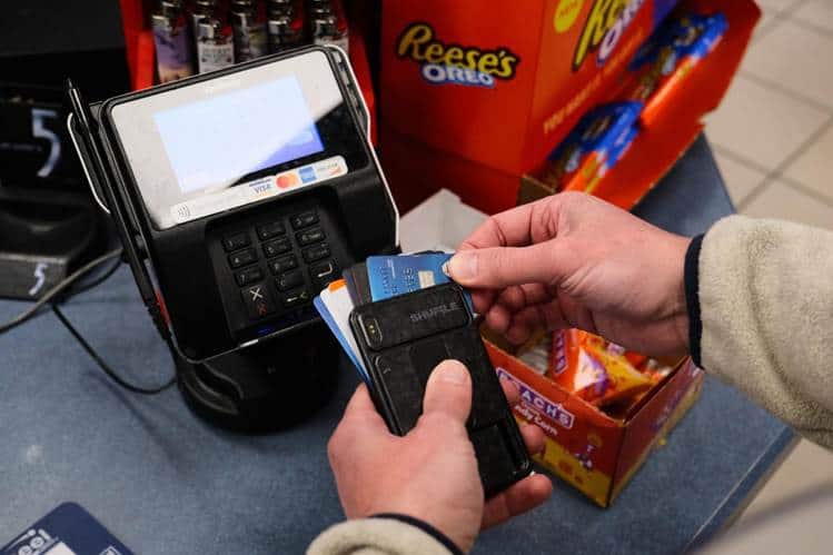 A person holds several credit cards and a phone wallet at a payment terminal, preparing to pay at a shop counter with sweets and snacks, including reese’s products, visible nearby. The sleek phone wallet stands out among traditional wallets for its convenience and modern design.