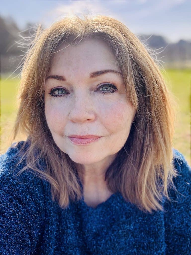 A portrait of a woman with shoulder-length hair wearing a blue jumper outdoors.