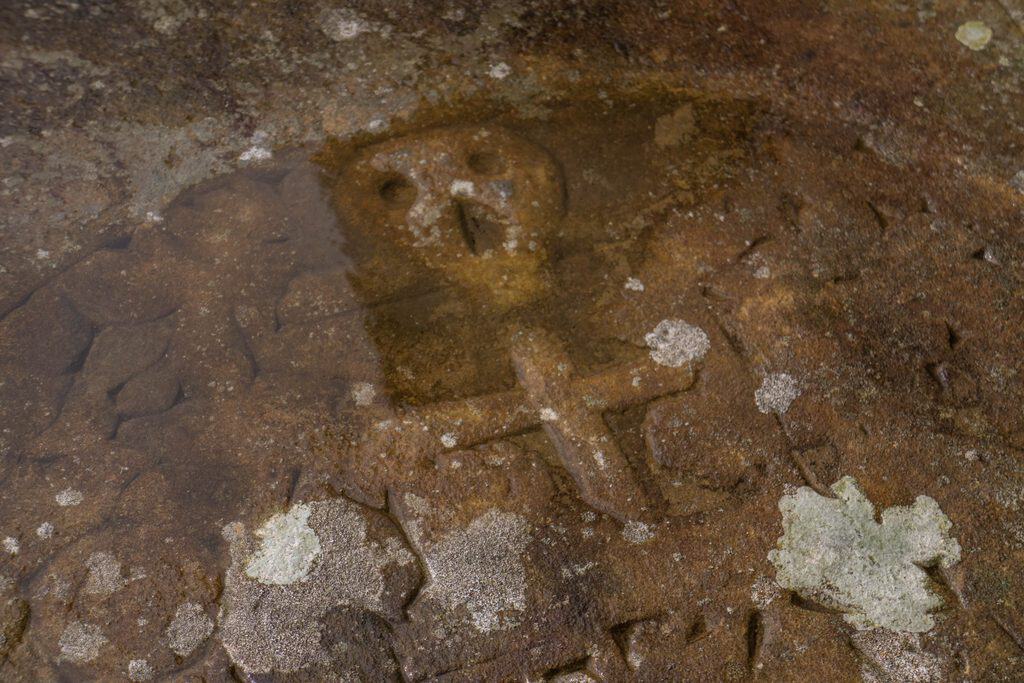 A stone carving of a skull and cross shape submerged in shallow water.