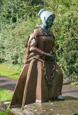 Bronze statue of a woman in a 16th-century cap and gown, kneeling with her hands in chains.