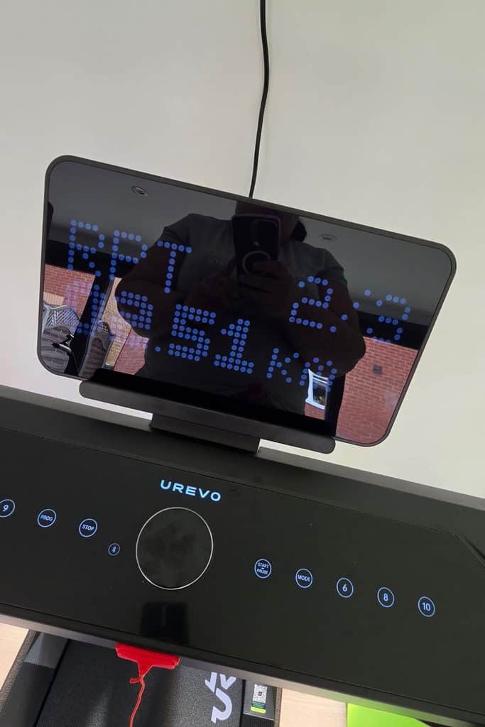 Urevo treadmill console displaying a digital time and distance readout, with a person reflected in the screen.
